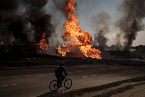 a person riding a bicycle with the view of a burning landscape